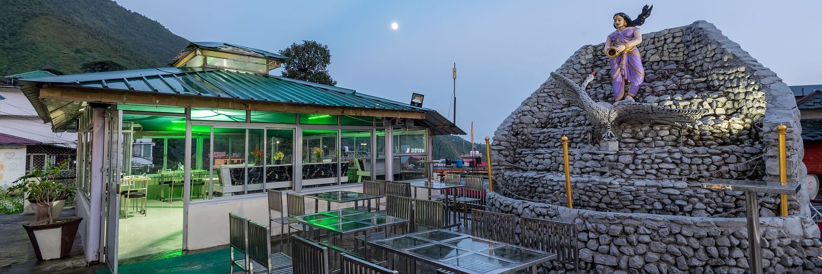 A view of an outdoor dining area at a resort with a stone fountain and a statue in the foreground -  DLS Meghavan Resort